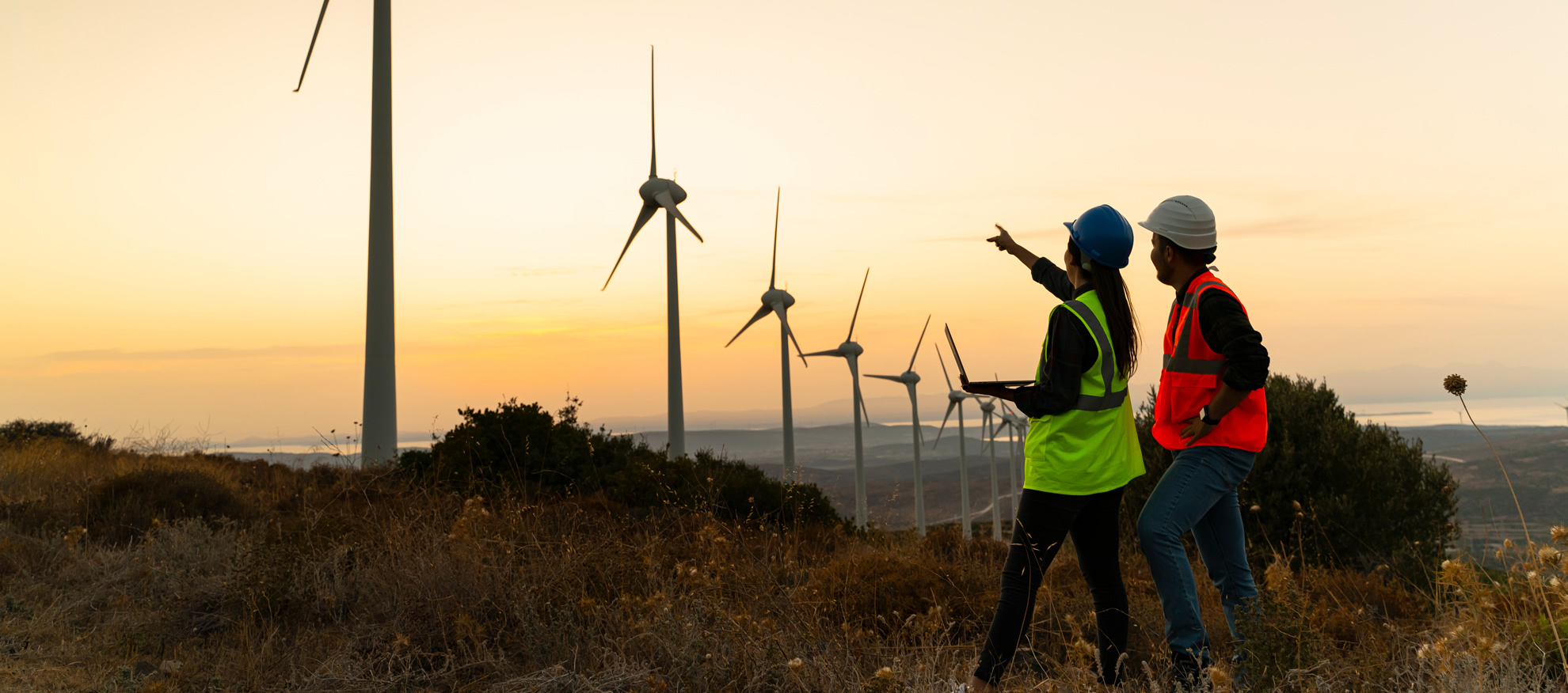 Engineers reviewing energy infrastructure beside wind turbines